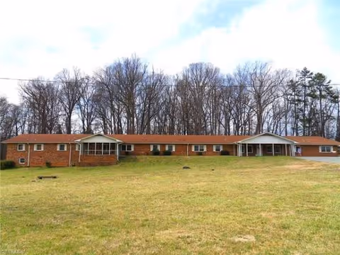 Long, single-story brick senior living building with a red roof and leafless trees in back.