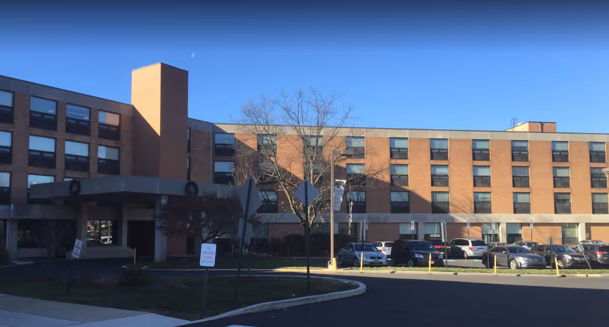 Brick, multi-story facility with a parking lot in front under a clear blue sky.