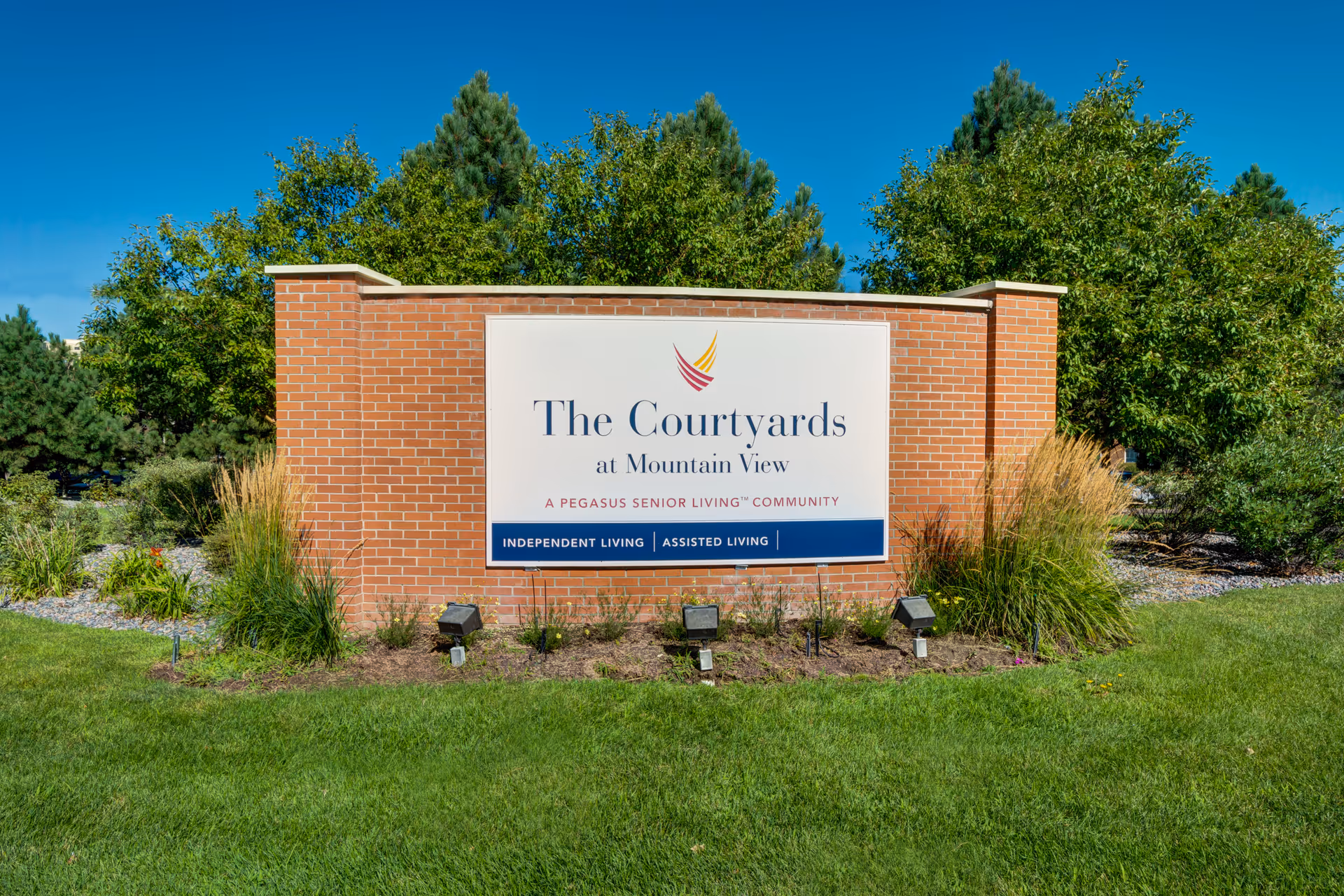 Brick entrance sign for The Courtyards at Mountain View senior living community surrounded by landscaped grass and trees.