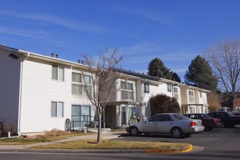 Two-story white senior living building with parked cars and leafless trees in front.