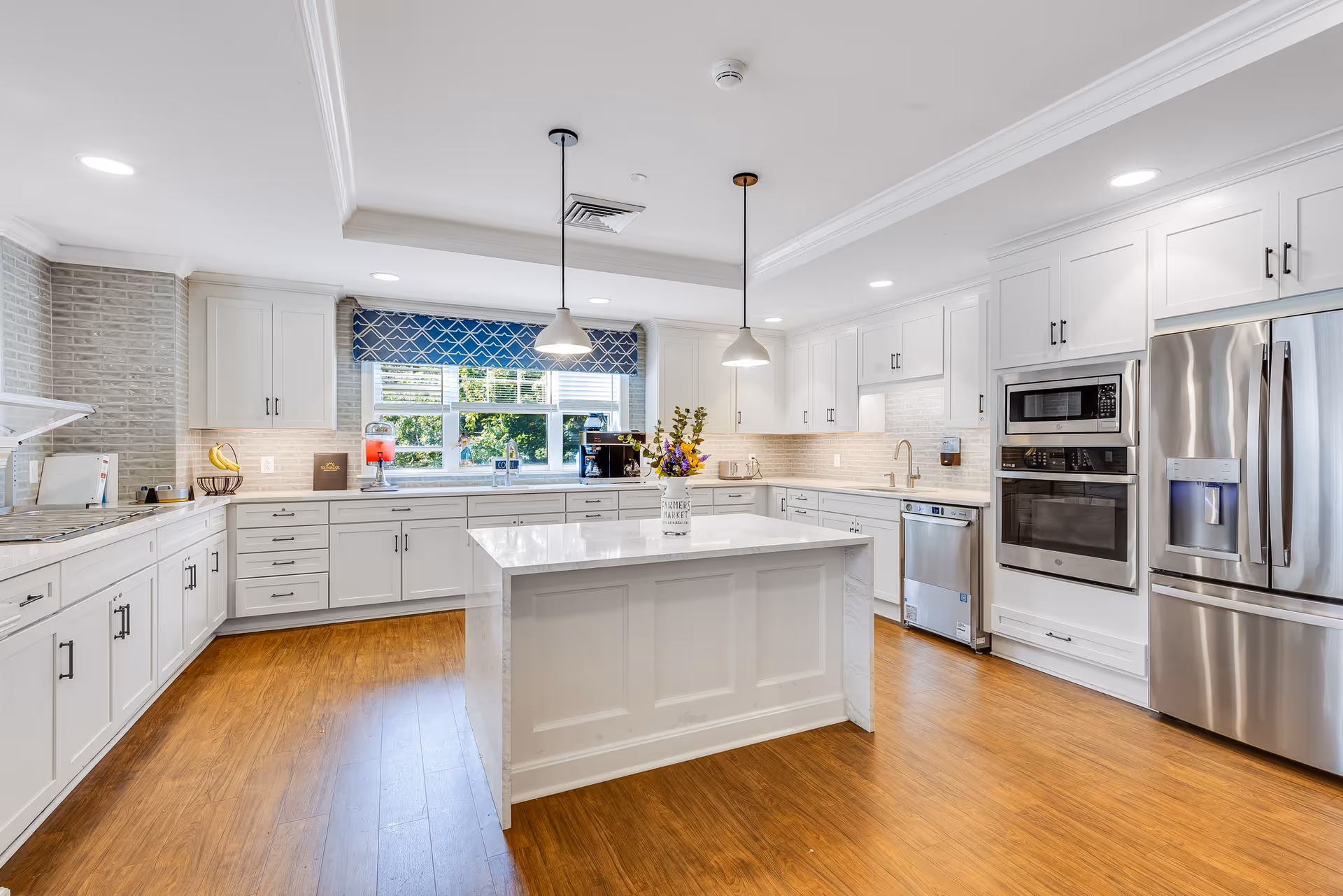 Bright modern kitchen with a central island, white cabinets, stainless steel appliances, and pendant lights.