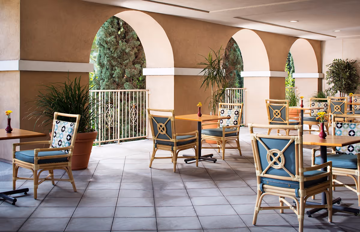 Covered outdoor patio dining area with tables, wicker chairs, potted plants and arched openings.