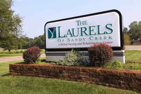 Outdoor sign for The Laurels of Sandy Creek with shrubs and brick planter