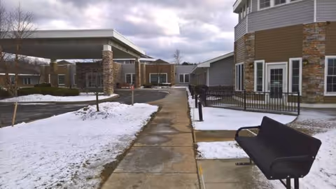 Snow covers the walkway and lawn outside Bristol Village, with the building entrance in view.