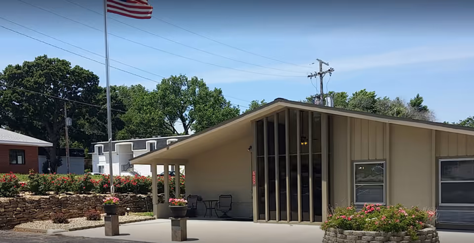 Oak Creek Senior Living exterior with slanted roof entrance, flagpole, and landscaped stone planters.