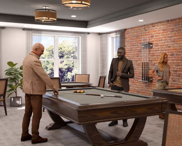Three people in a recreational room with a pool table. One man is preparing to take a shot while another man and a woman watch. The room has large windows with views of trees outside, a brick accent wall with pool cues mounted, and modern ceiling lights.