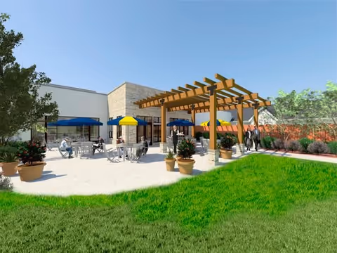 Outdoor patio area at Bryant House with tables and chairs under blue and yellow umbrellas, a wooden pergola, potted plants, green grass, and people sitting and standing around.
