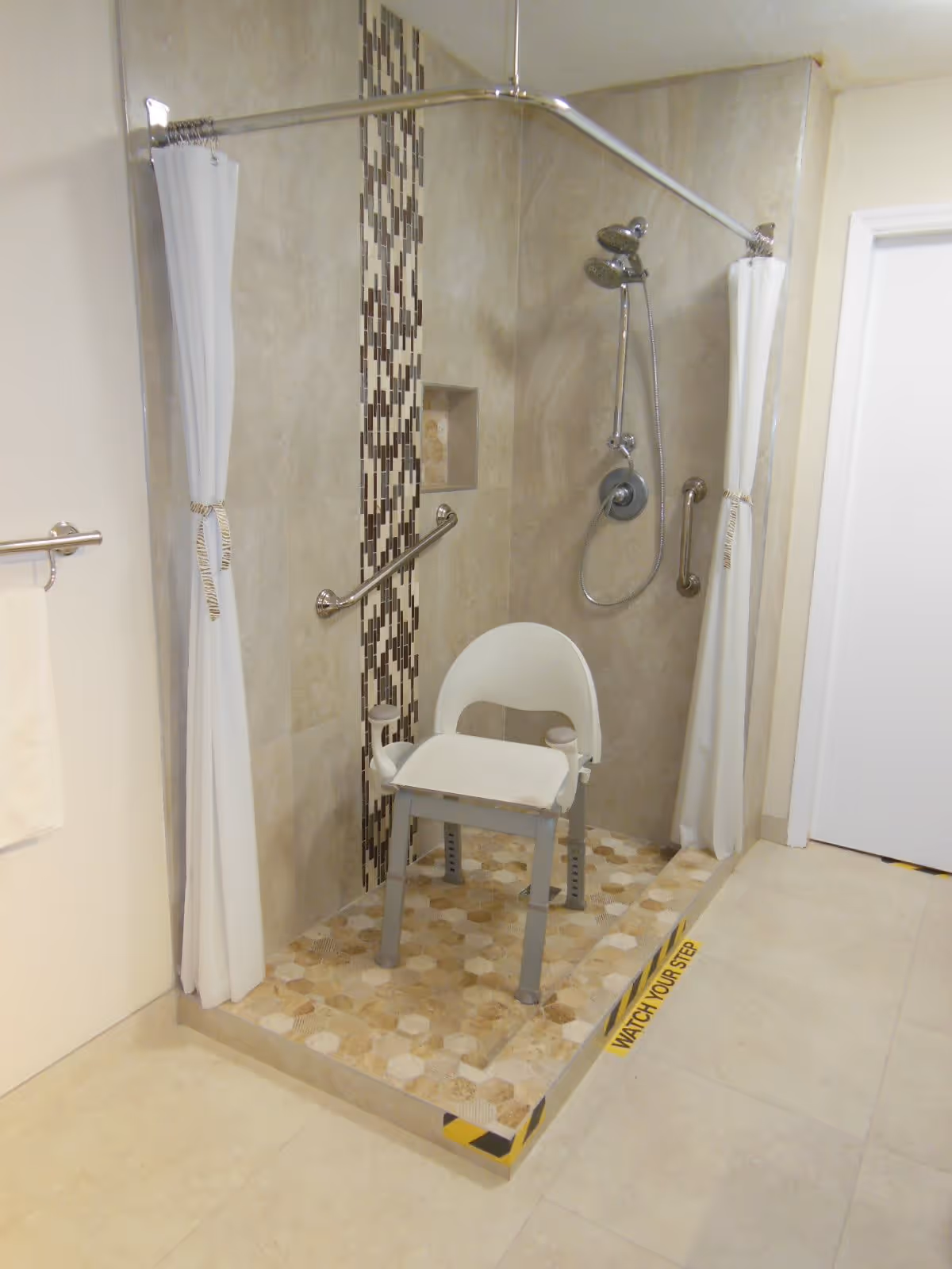 Accessible walk-in shower with a shower chair, grab bars, a handheld shower head, and curtains.