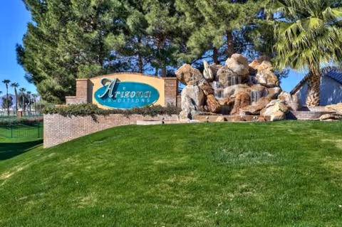 Entrance sign for Arizona Traditions Senior Living with rocks, lawn, and palm trees.