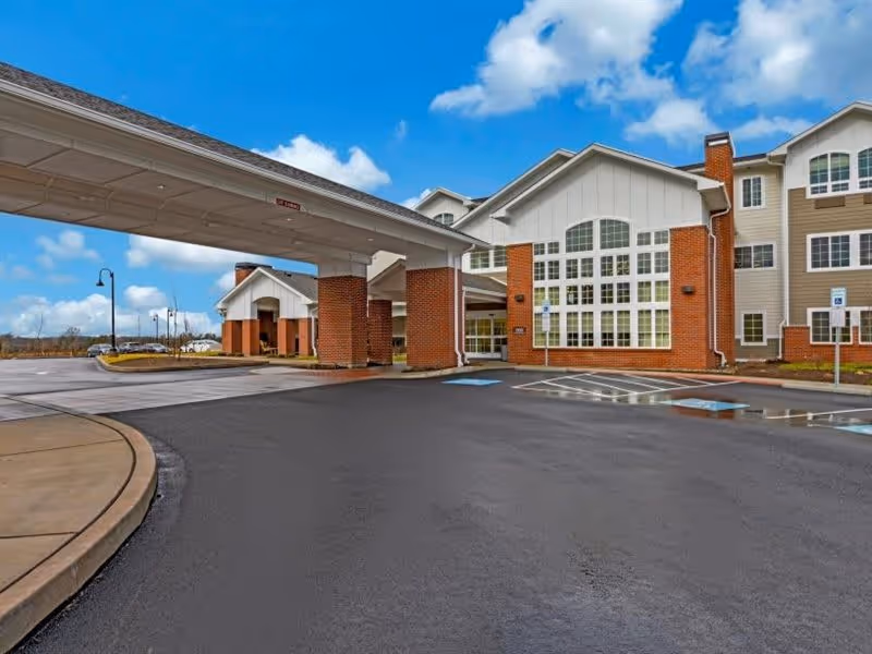 Exterior view of Morningside House of Towamencin showing the front entrance with a covered drop-off area supported by brick columns, adjacent parking spaces including handicapped spots, and a multi-story building with large windows under a partly cloudy sky.