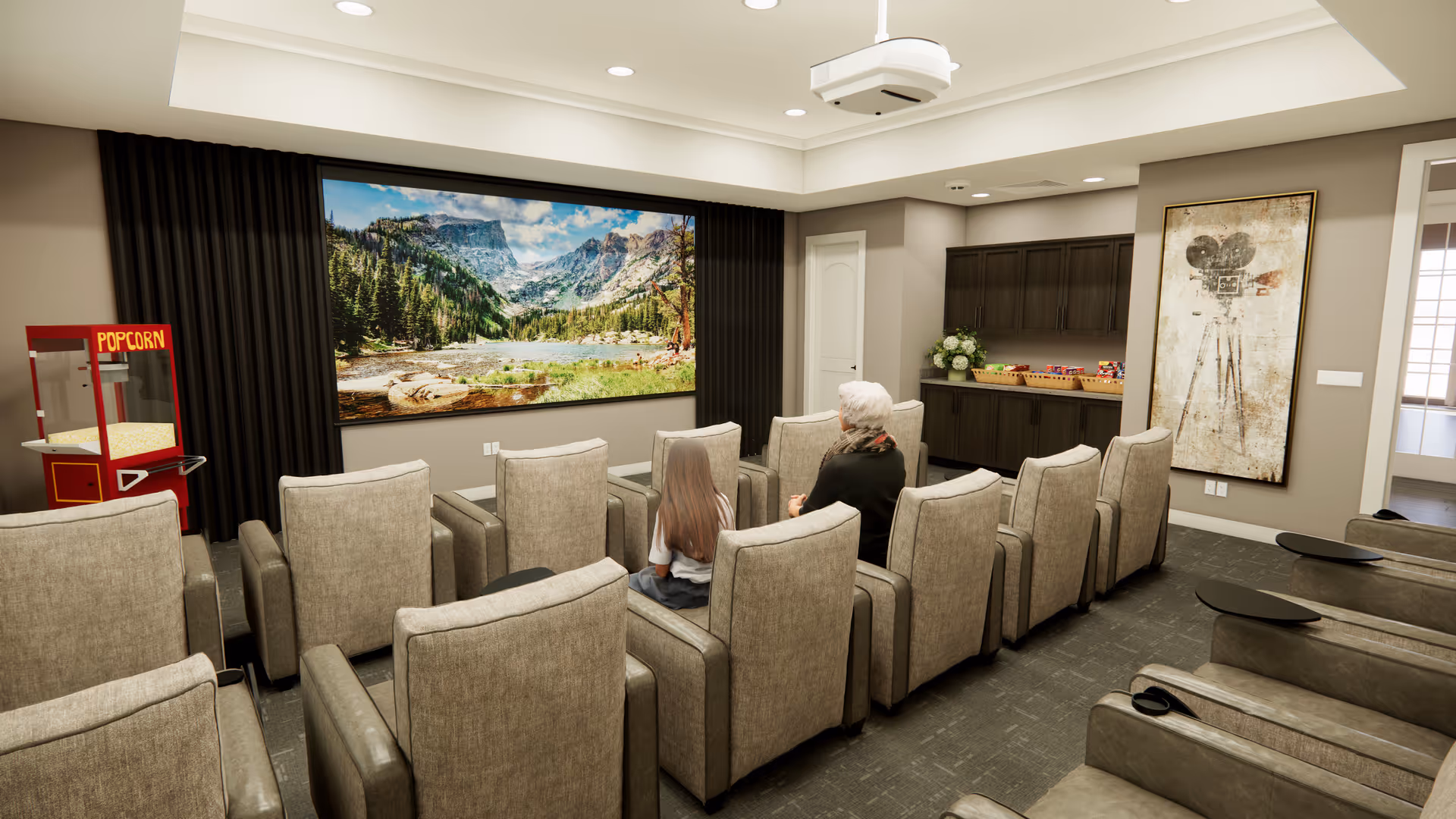 A small theater room with two rows of beige recliner chairs facing a large screen displaying a scenic mountain and forest landscape. Two people, an elderly woman and a young girl, are seated in the chairs. To the left, there is a red popcorn machine. The room has recessed lighting, dark curtains framing the screen, and a cabinet with snacks on the right side. A vintage movie camera artwork is hung on the wall.