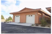 Front exterior of a single-story villa with two garage doors and desert landscaping.