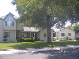 Exterior view of a single-story senior living facility with lawn and tree.