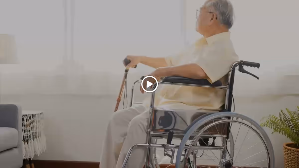 An older adult seated in a wheelchair holding a cane in a bright living room setting.