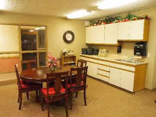 Common dining area with round table, chairs, and kitchenette along wall.