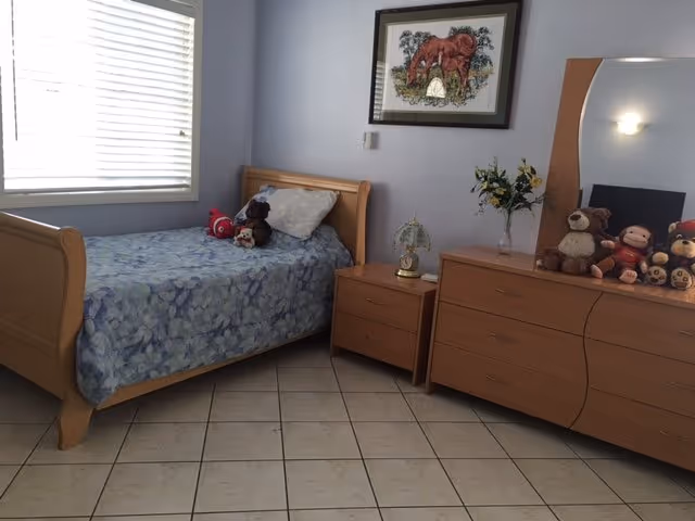 A tidy bedroom in Sunshine's Place II with a single bed, dresser, window, and toys.