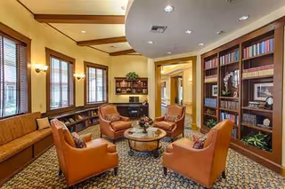 Warm lounge area with leather chairs, sofa, coffee table, and bookshelves in a cozy waiting room.
