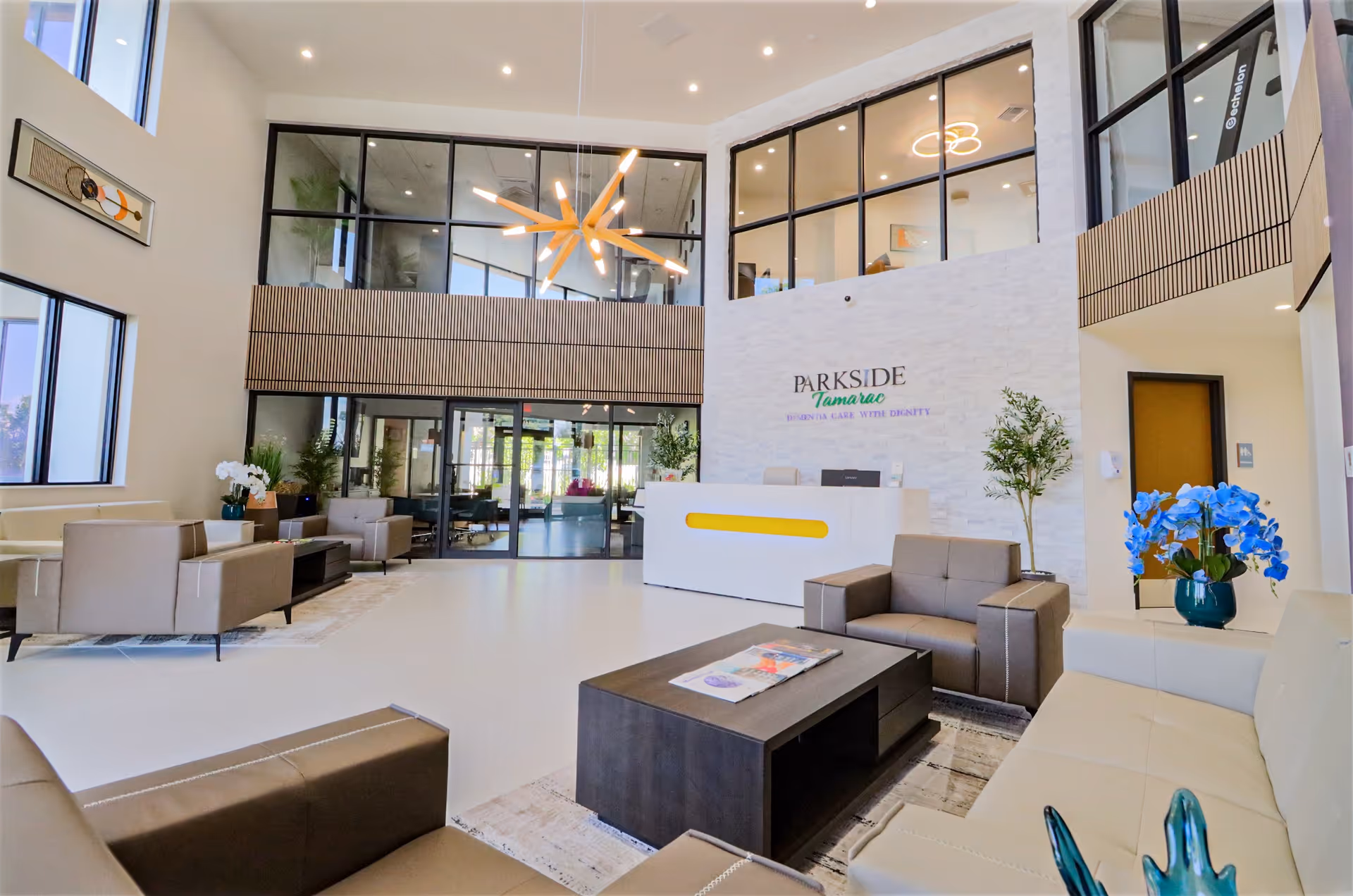 Bright modern reception lobby with seating, a front desk reading 'Parkside Tamarac', large windows, and contemporary lighting fixtures.