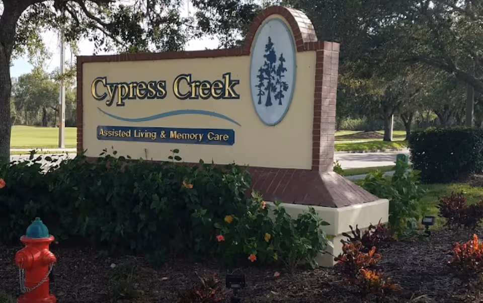 Cypress Creek Assisted Living sign in front of landscaped shrubs and trees.