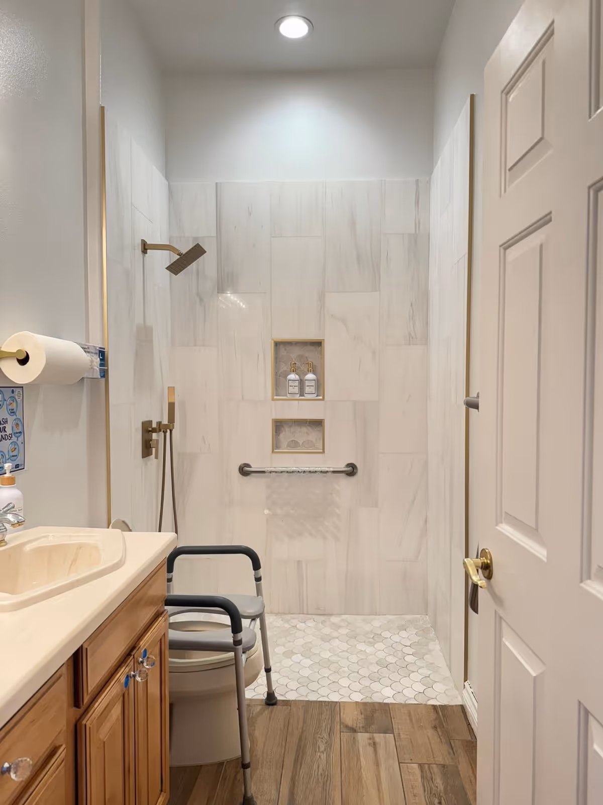 Accessible bathroom with a walk-in tiled shower, grab bar, shower chair, and a wooden vanity with sink.