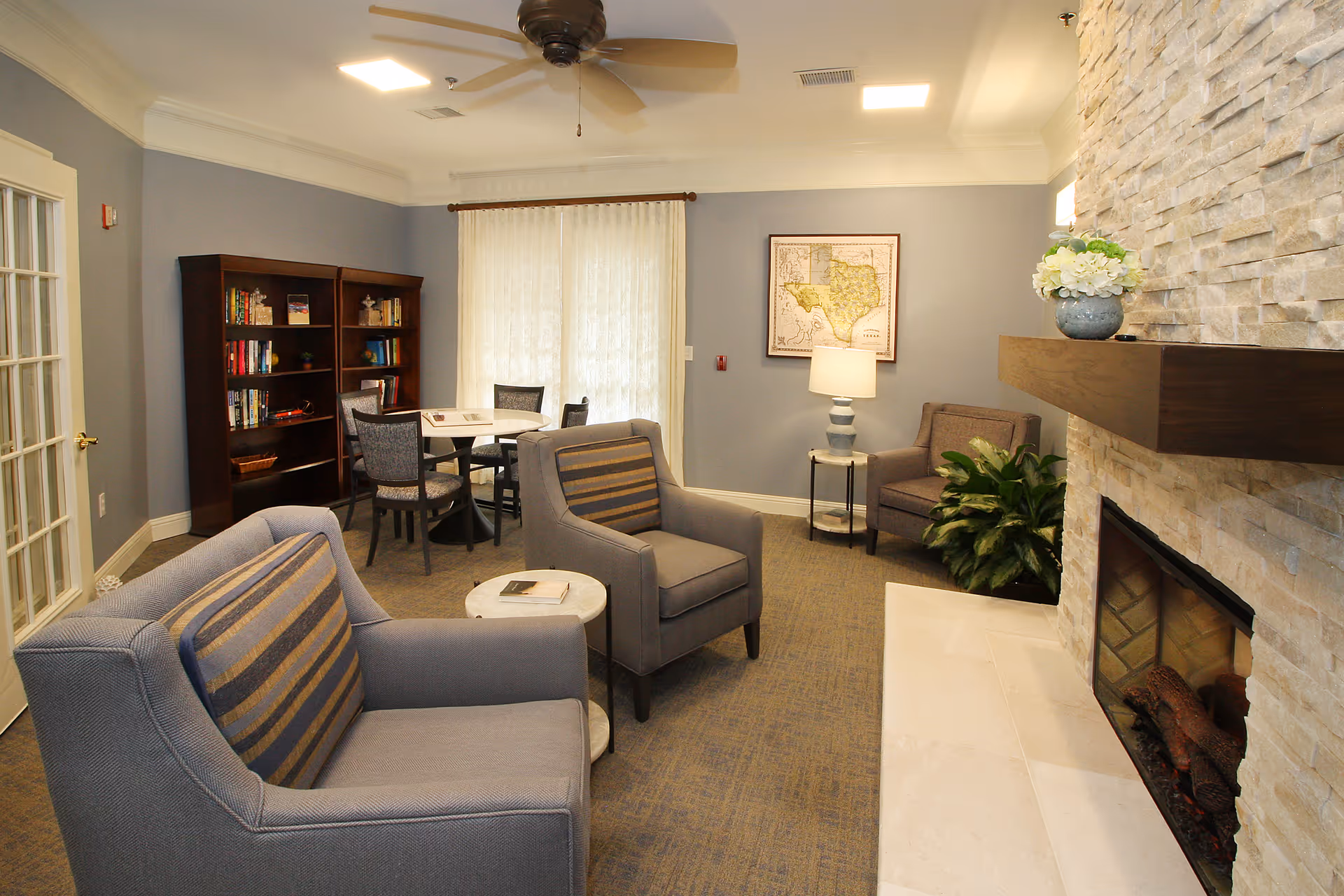 Cozy common sitting room with upholstered armchairs, a stone fireplace, bookshelf, round table, and lamp.
