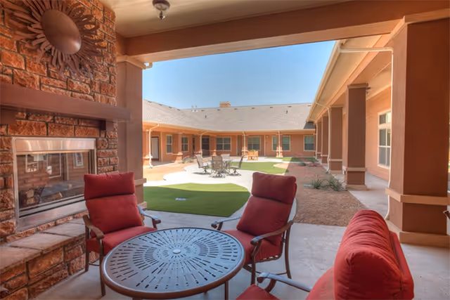 Covered courtyard seating area with red cushioned chairs, a round metal table and a stone fireplace opening onto an open courtyard with patio tables.