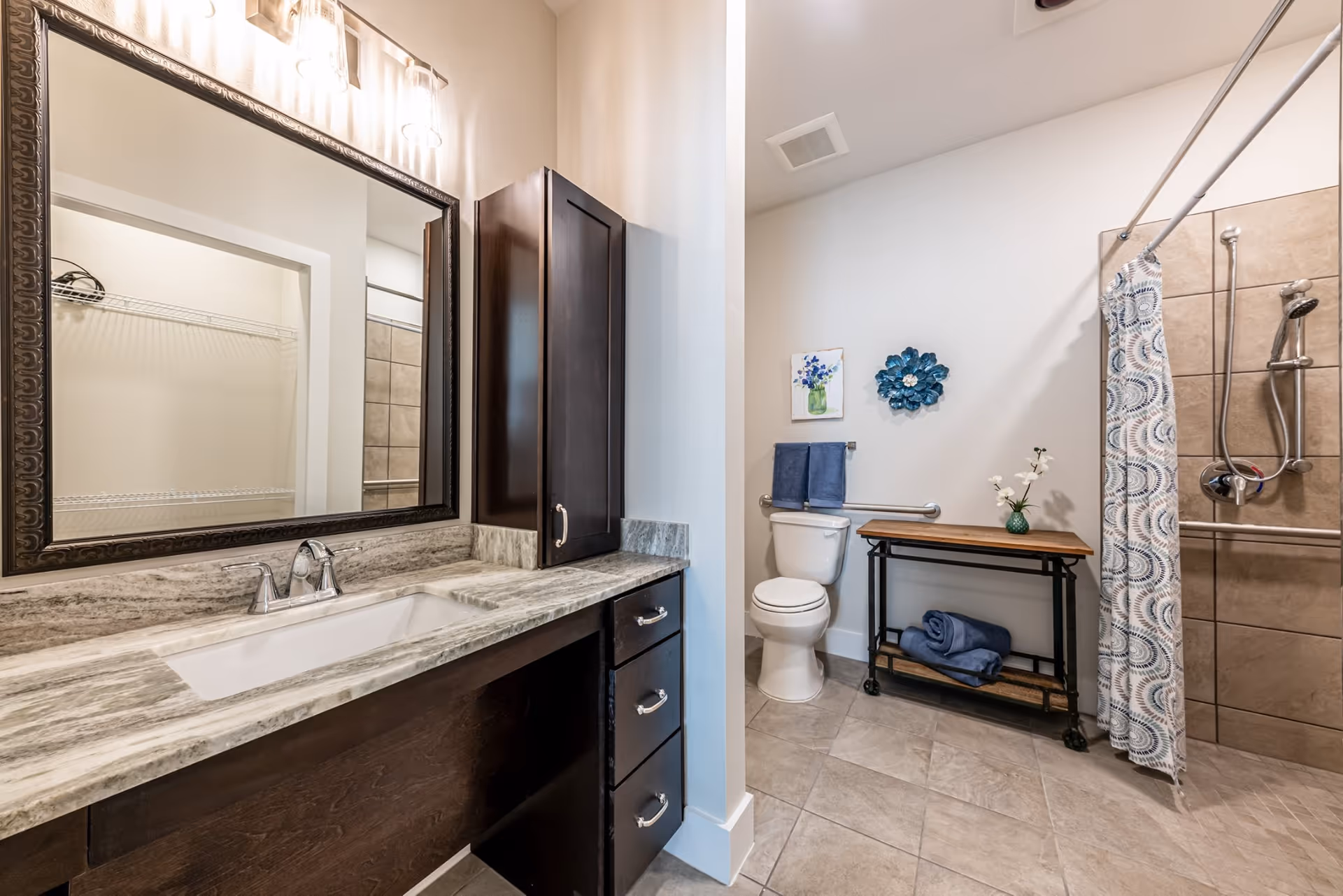 Modern bathroom with dark vanity, oversized mirror, toilet, and tiled shower stall.