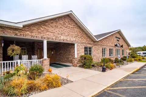 Front entrance of a single-story brick senior living building with a covered porch, walkway, and landscaped beds.