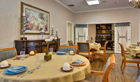 Dining room with round tables set with place settings, wooden chairs, a sideboard and wall art.