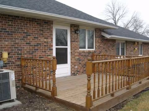 Brick senior living building with a wooden deck and railing at the entrance.