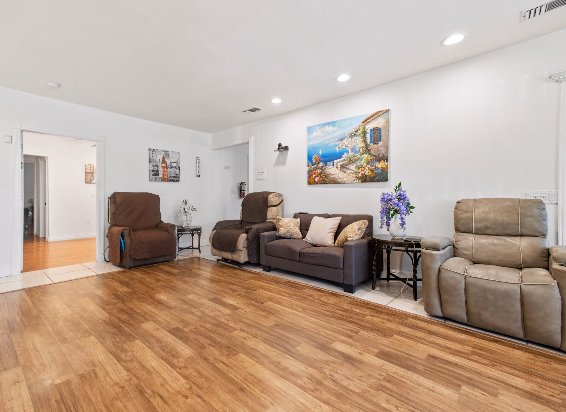 Bright communal living room with multiple recliners, a sofa, side tables, and a coastal painting on the wall.