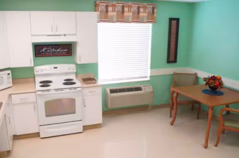 Bright mint-green kitchen with white cabinets, stove, window, and dining table.