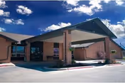 Exterior view of a single-story brick building with a covered entrance supported by brick columns under a blue sky with scattered clouds.