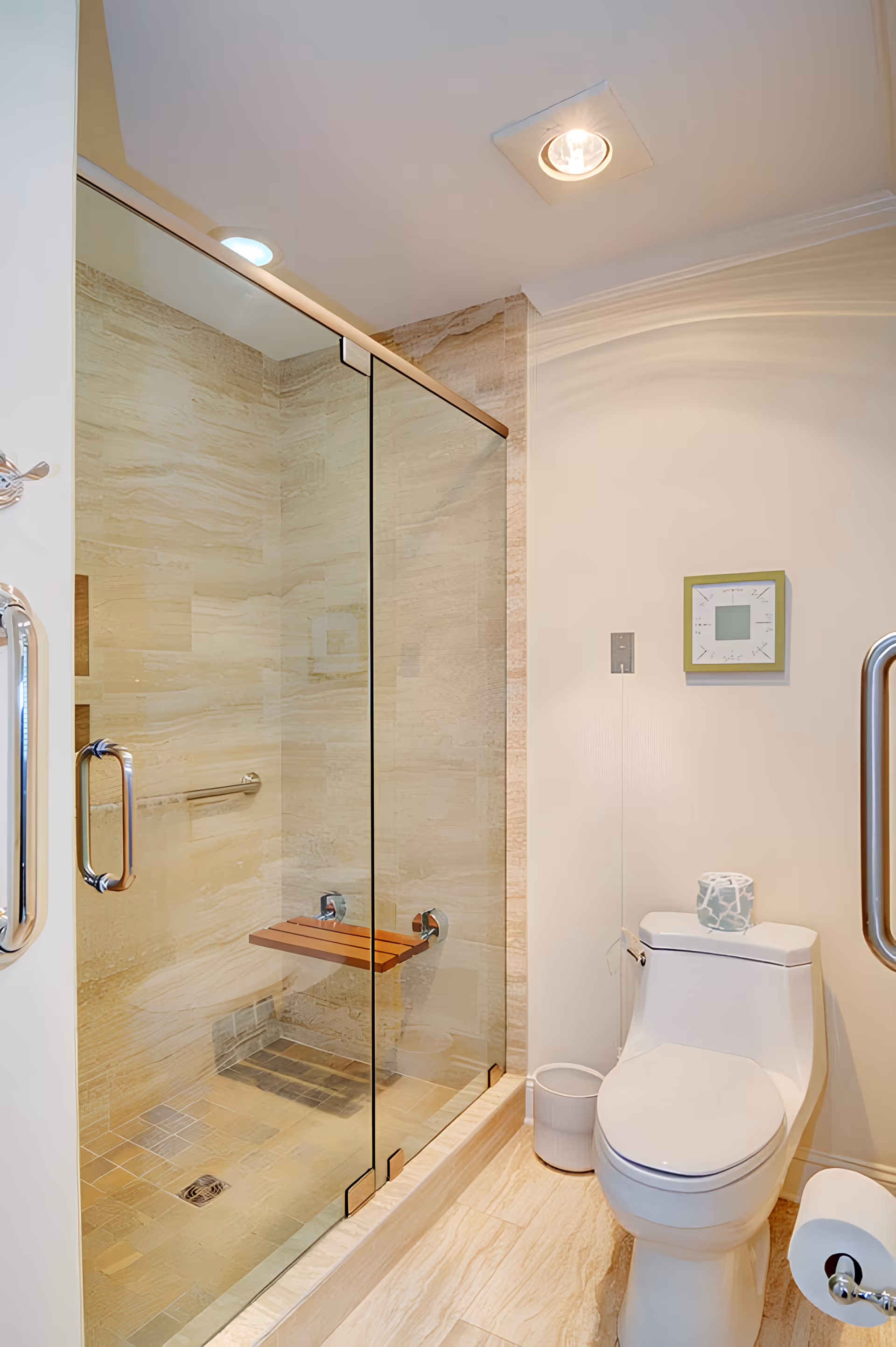 A modern bathroom featuring a glass-enclosed shower with beige stone tiles and a wooden fold-down seat inside. Next to the shower is a white toilet with a decorative tissue box on top, a small trash bin beside it, and a wall-mounted square clock above. The floor is tiled in a light beige color.