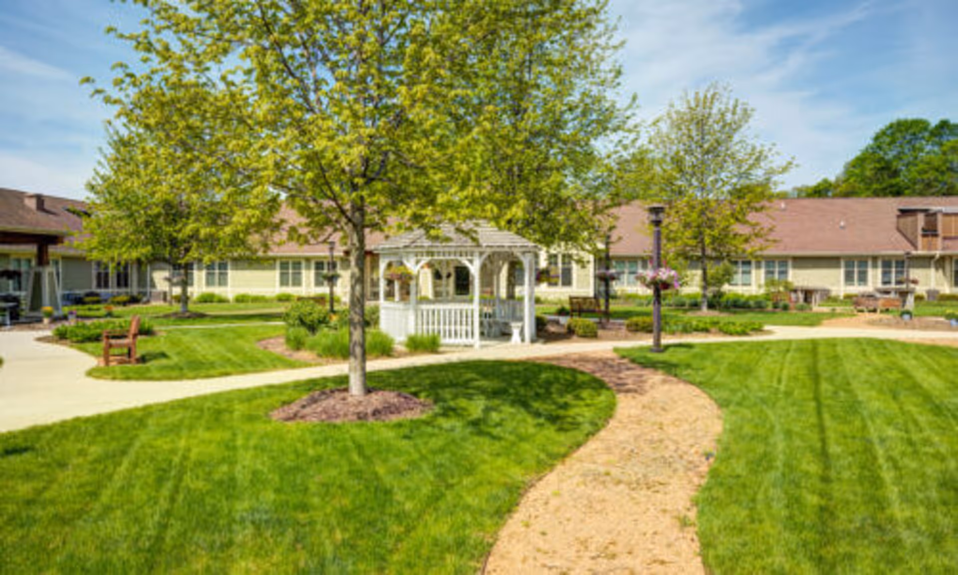 Well-maintained courtyard with a white gazebo, walking paths, benches, trees, and a surrounding single-story building.