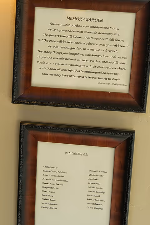 Two framed memorial plaques on a wall, one titled "MEMORY GARDEN" with a poem and the other titled "IN MEMORY OF" listing names.
