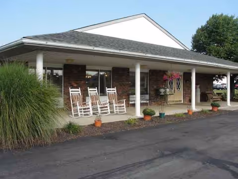 Senior care center exterior with brick walls and white rocking chairs on covered porch.