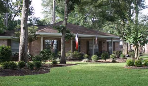 Brick-front senior living facility with manicured lawn, shrubs, and trees.