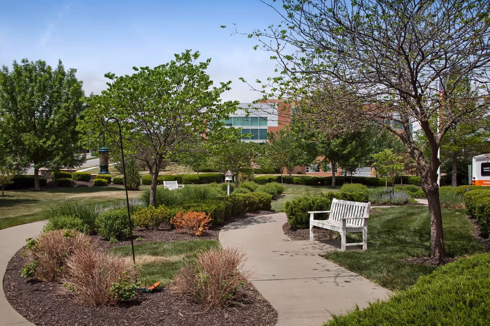 Well-maintained outdoor garden path with benches, trees, and a building in the background.