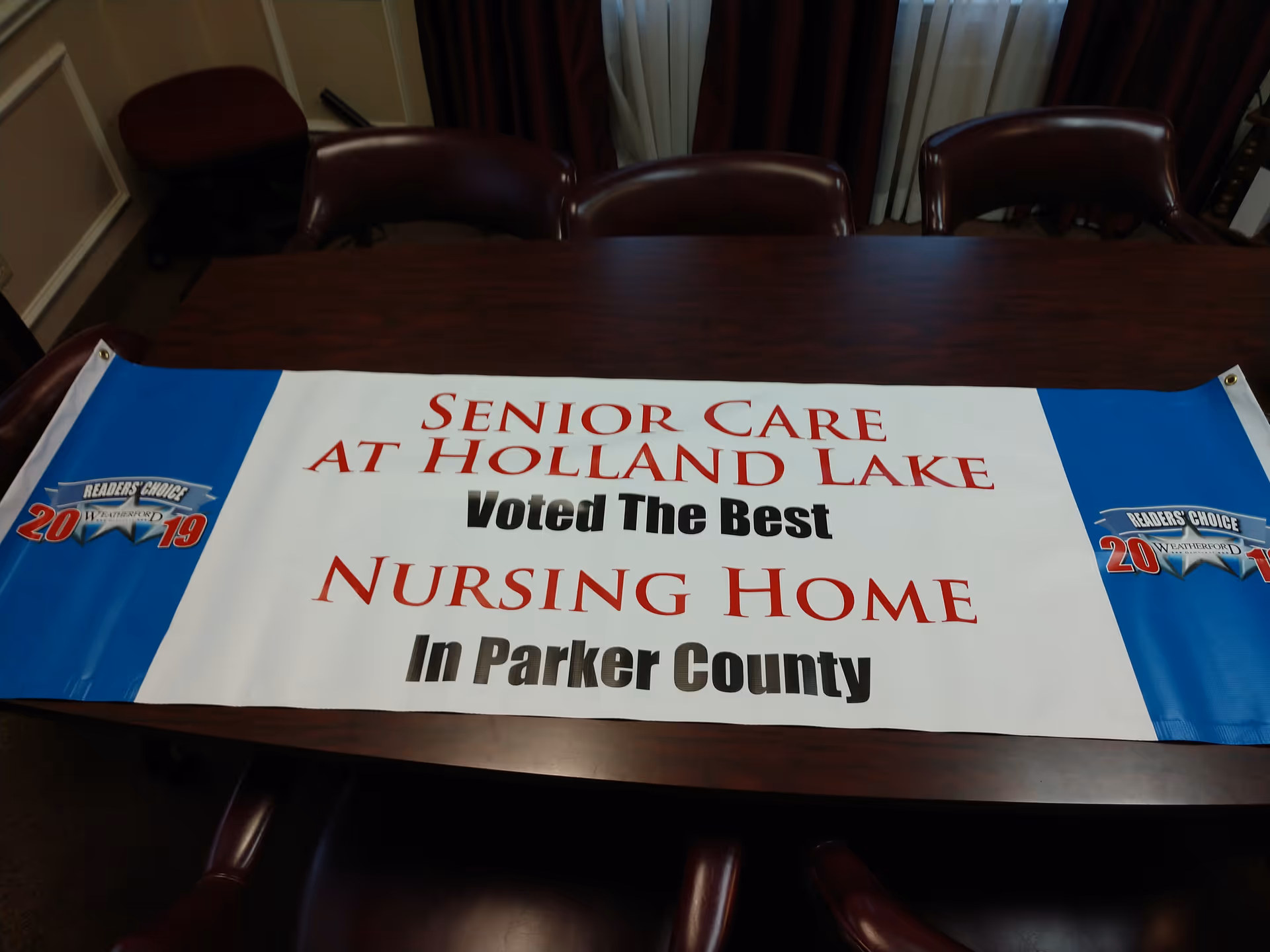 A banner on a conference table reading 'Senior Care at Holland Lake Voted The Best Nursing Home in Parker County.'
