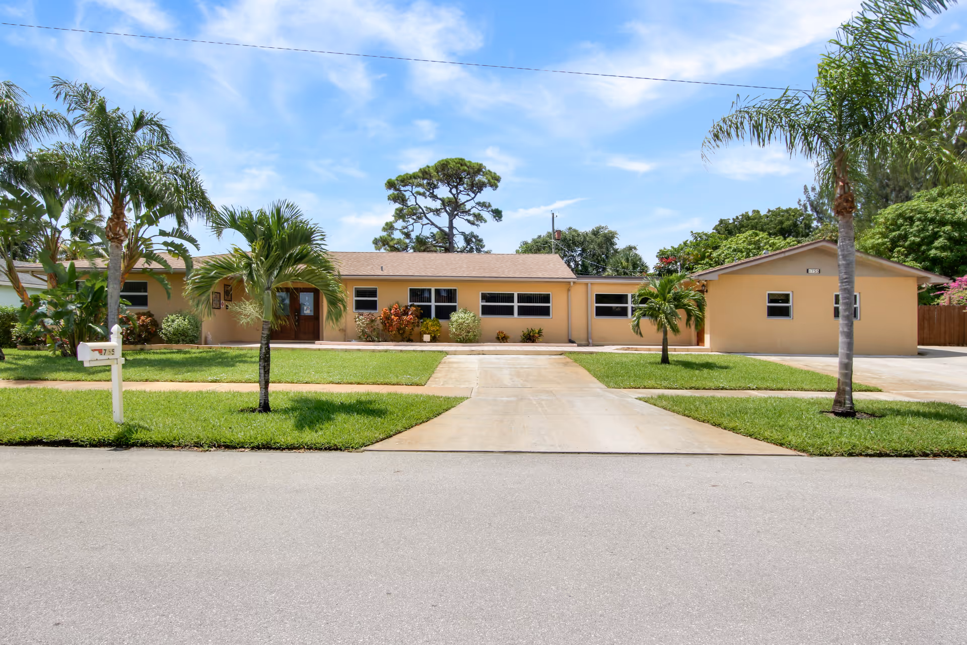 Single-story peach-colored building with a central driveway, palm trees, and a manicured lawn under a blue sky.