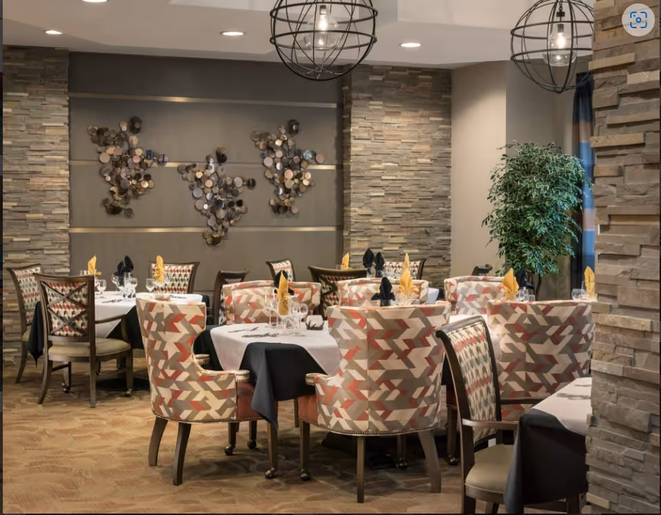 Elegant dining room with tables set for service, patterned upholstered chairs, stone accent walls and spherical pendant lights.