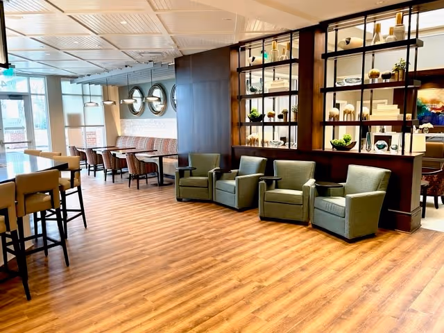 Spacious, well-lit communal lounge and dining area with chairs, booths, shelving displays, and wood flooring.