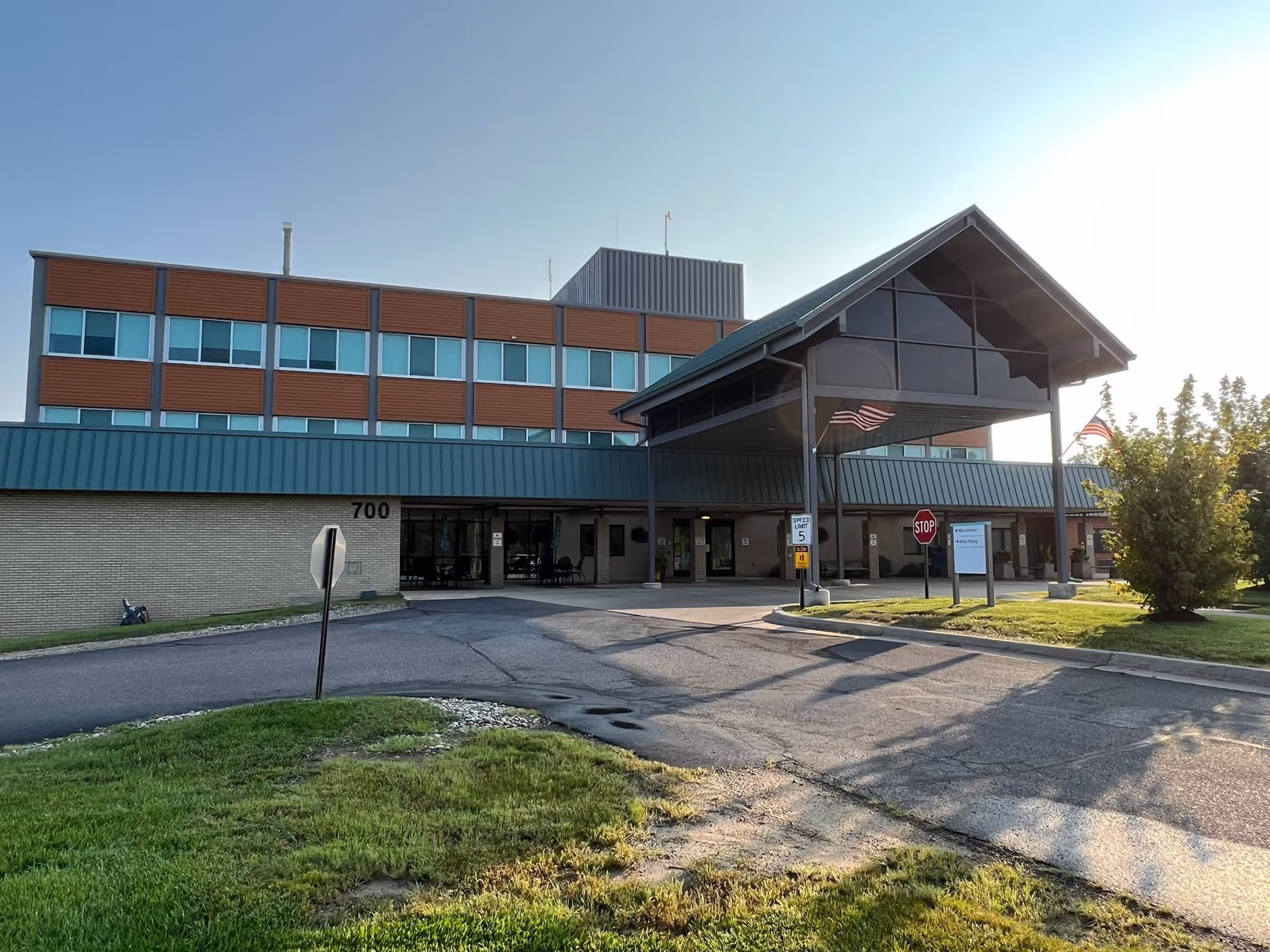 Front entrance of a multistory nursing center with a covered porte-cochère, American flags, and the street number 700 visible.