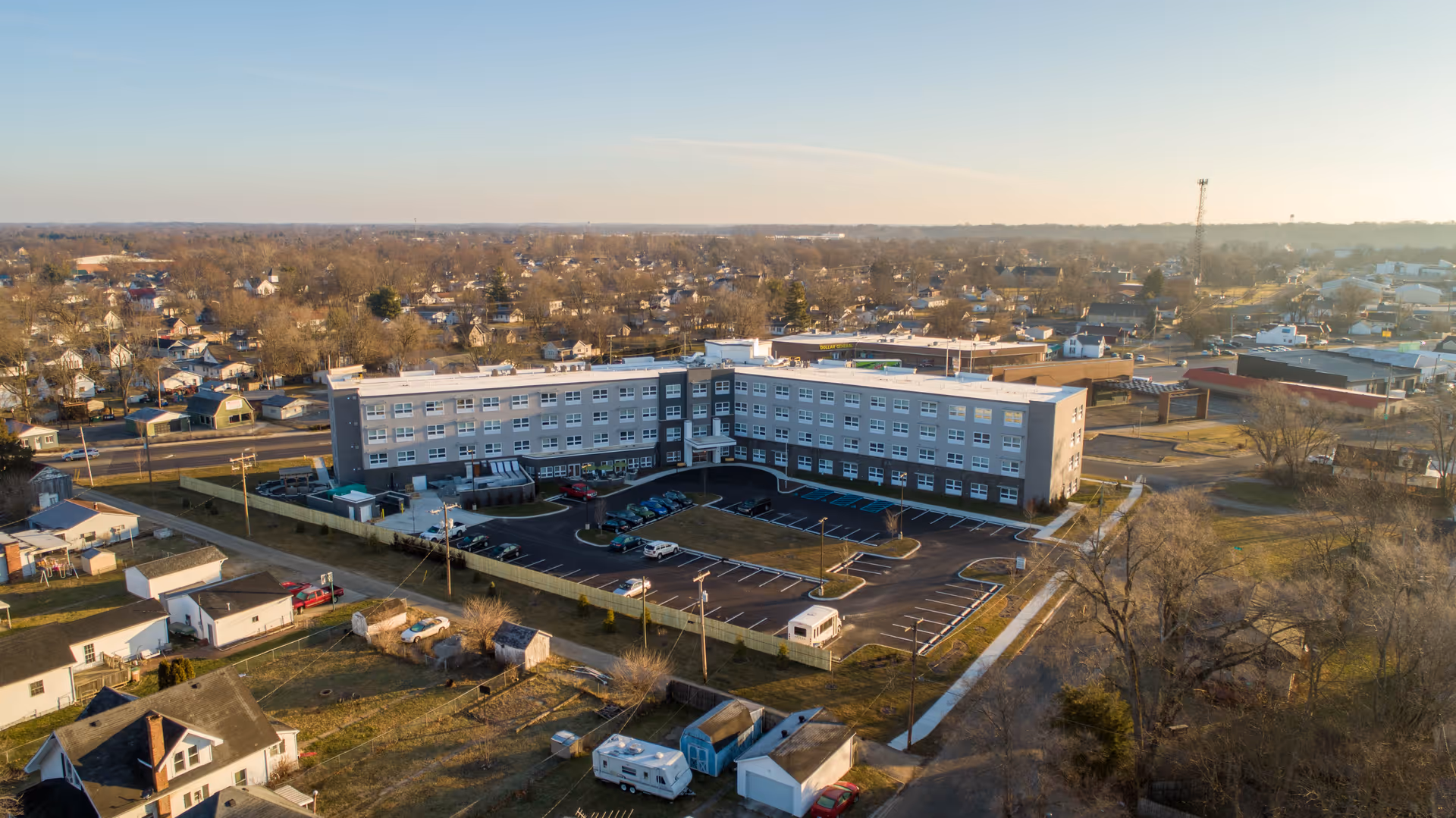 Aerial view of Vivera Senior Living of Columbus, a large multi-story senior living facility surrounded by a parking lot and residential neighborhood under a clear sky.