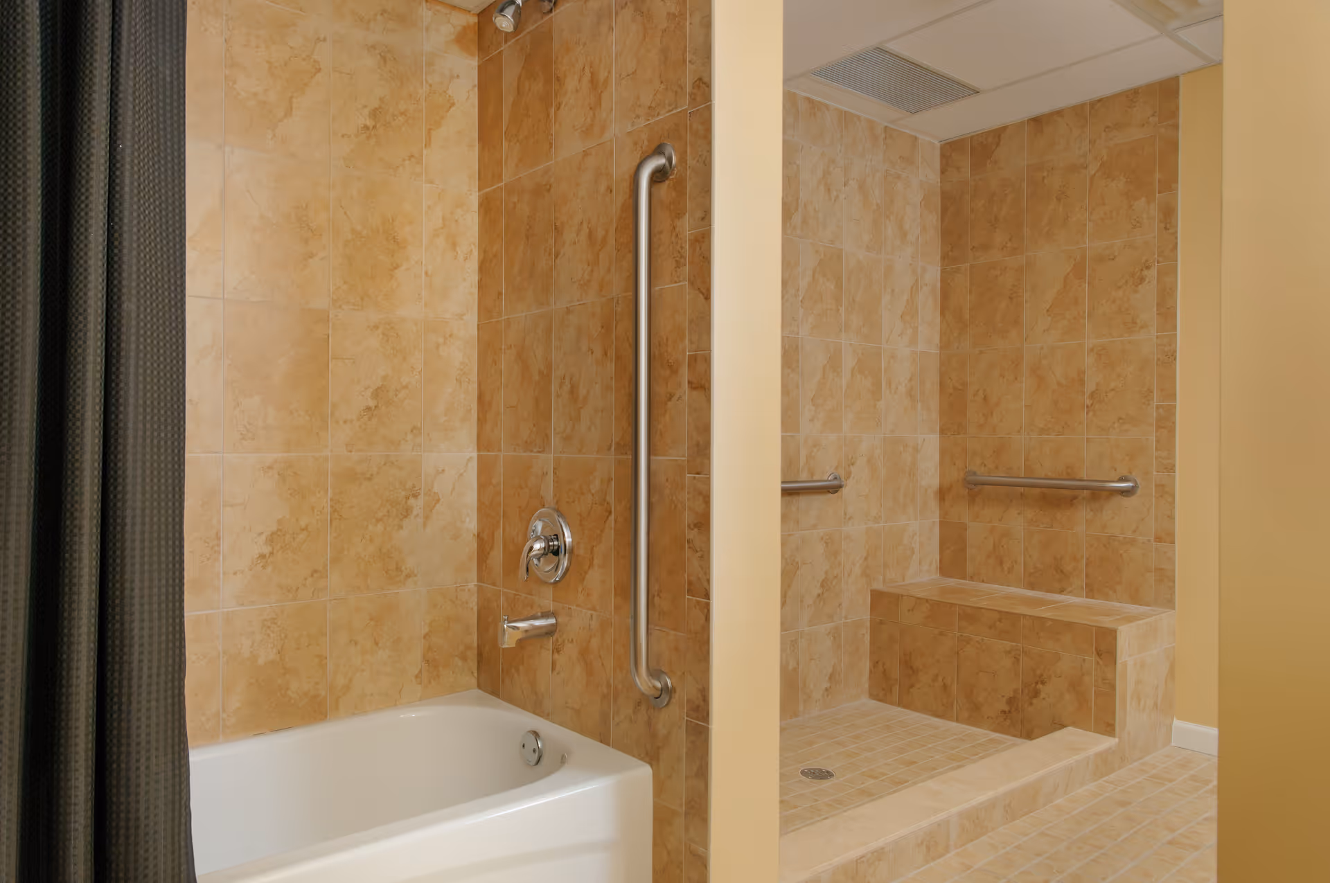 Tiled accessible bathroom with a bathtub, a walk-in shower with a built-in bench, and stainless steel grab bars.