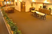 Spacious interior common area with table, chairs, plants, and cabinet in a senior living facility.