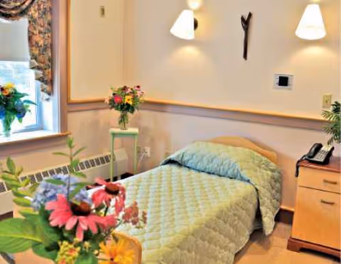 Bedroom at Mount St. Rita Health Centre with a neatly made bed, flowers, and bedside furniture.