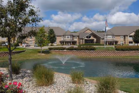 Exterior view of a senior living facility with a pond fountain and landscaped grounds.