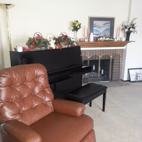 Cozy living room with leather chair, upright piano, and decorated fireplace mantel.